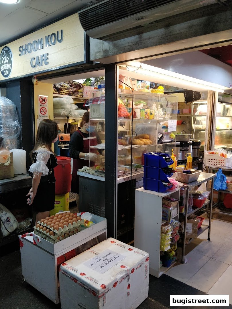 A view of Shoon Kou Cafe's entrance, showing staff and food items displayed.