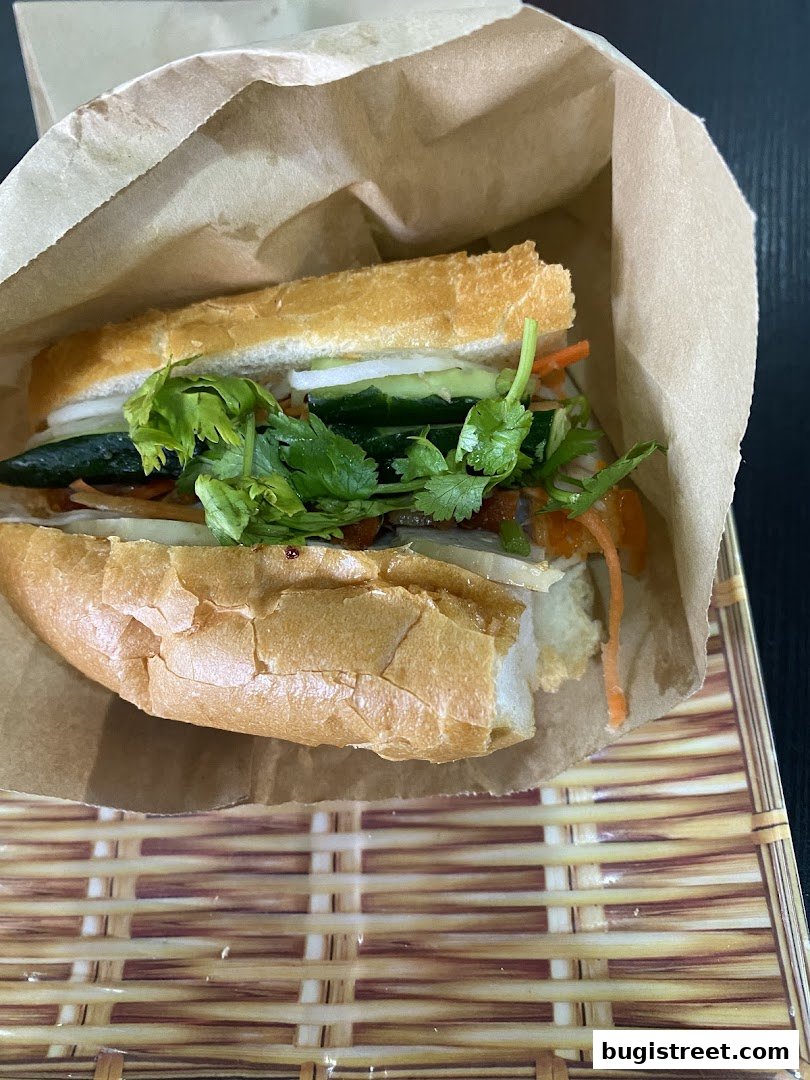 A delicious banh mi sandwich with fresh cilantro, cucumber, and pickled carrots in a paper wrapper.
