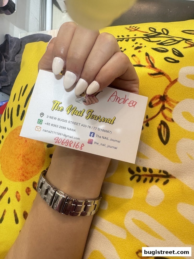 A hand with freshly painted nails holds a business card for 'The Nail Journal'.
