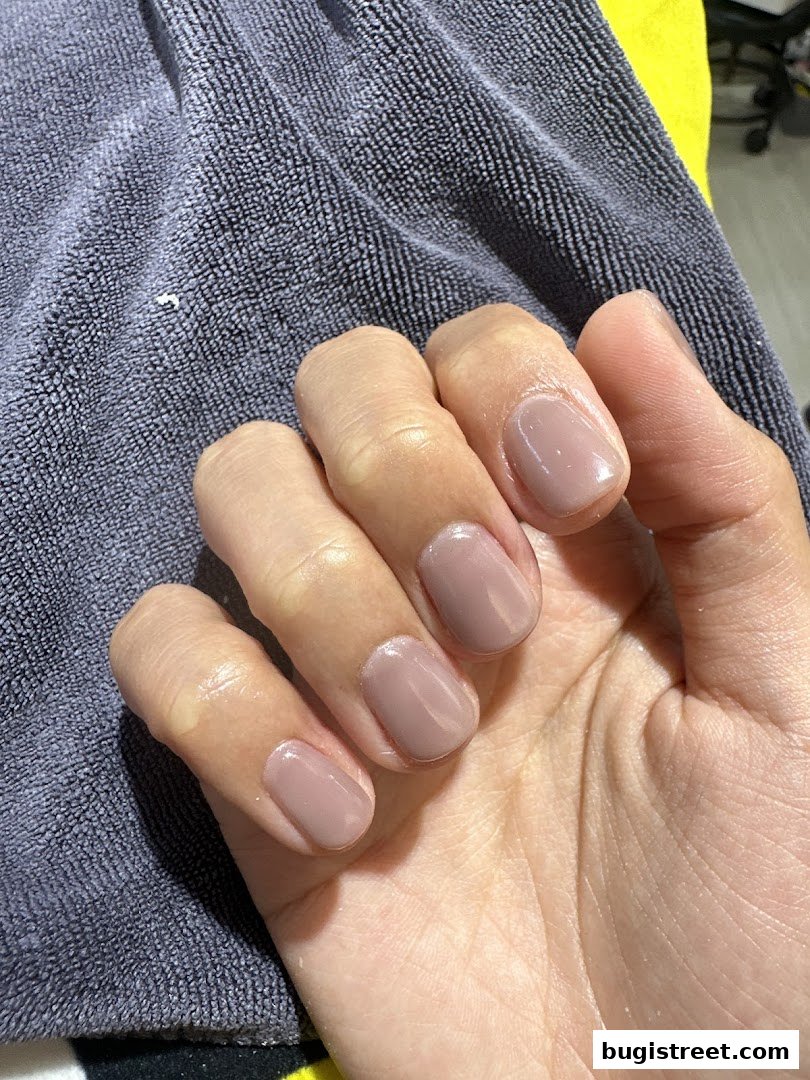 A close-up of a hand with perfectly manicured, nude-colored nails resting on a textured gray towel.
