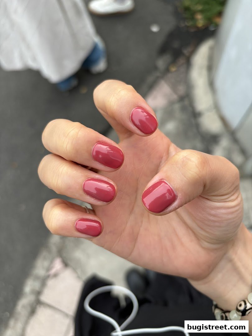 A close-up of a hand with perfectly manicured nails painted in a rich, rosy hue.