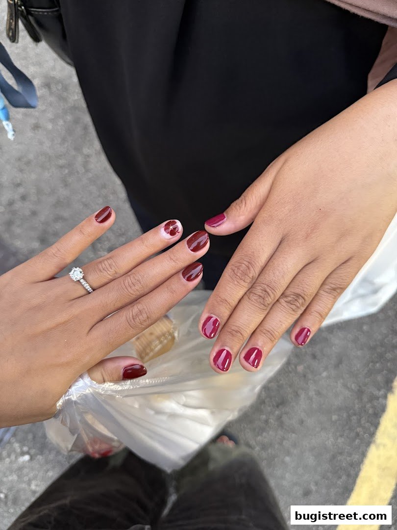 Close-up of two hands showcasing beautifully manicured nails with a deep red polish and subtle floral art.