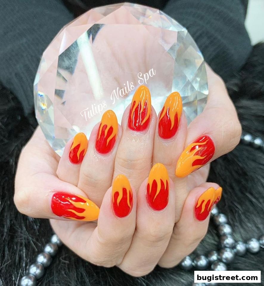 A close-up of hands with vibrant flame-designed nails, holding a crystal.