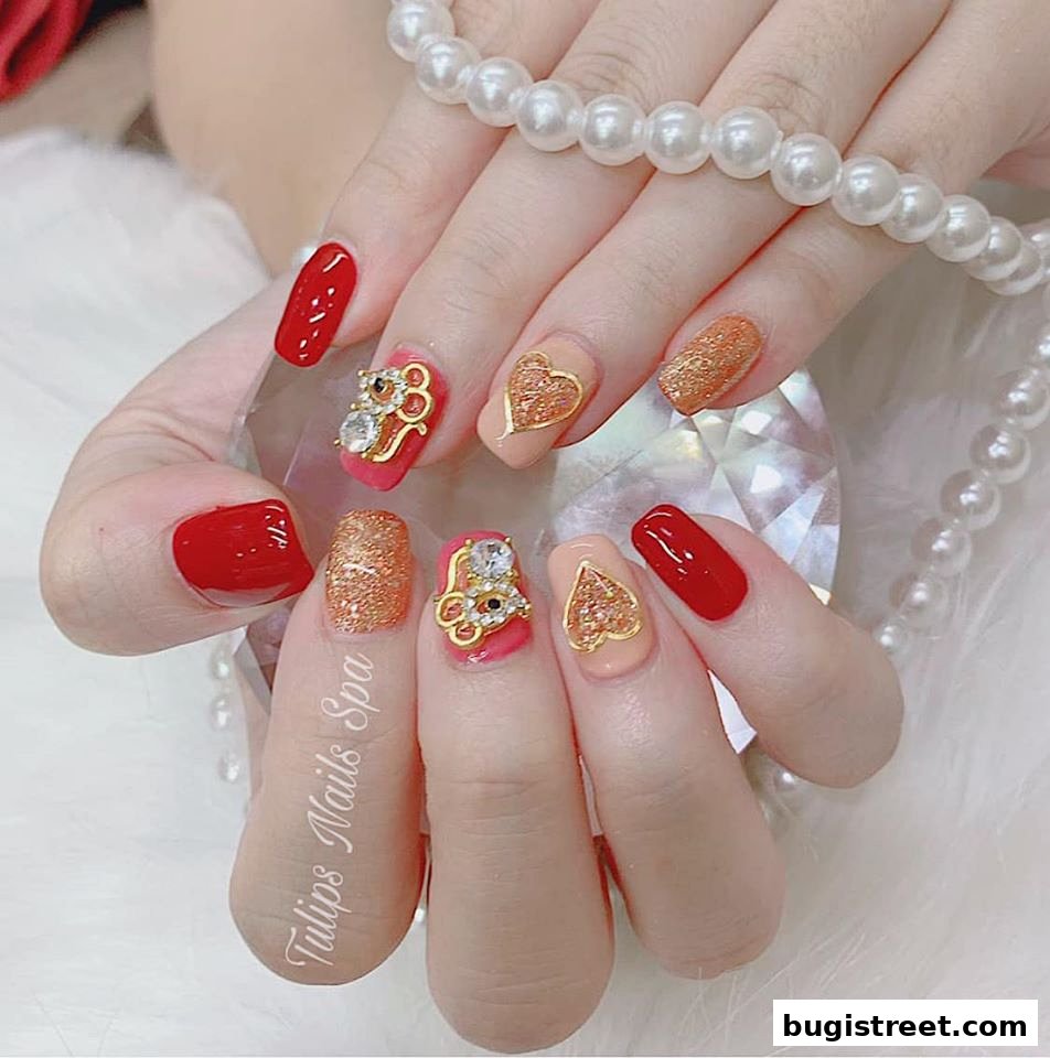 Close-up of hands with elaborately decorated nails featuring red, gold glitter, and heart designs.
