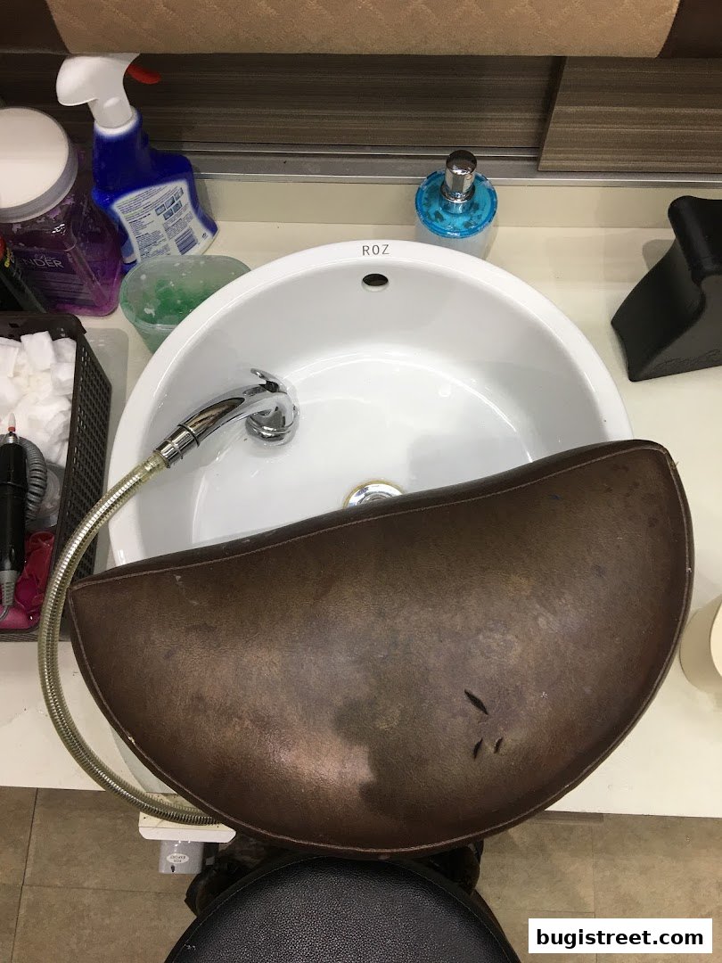 A nail spa sink area with various cleaning supplies and a footrest.