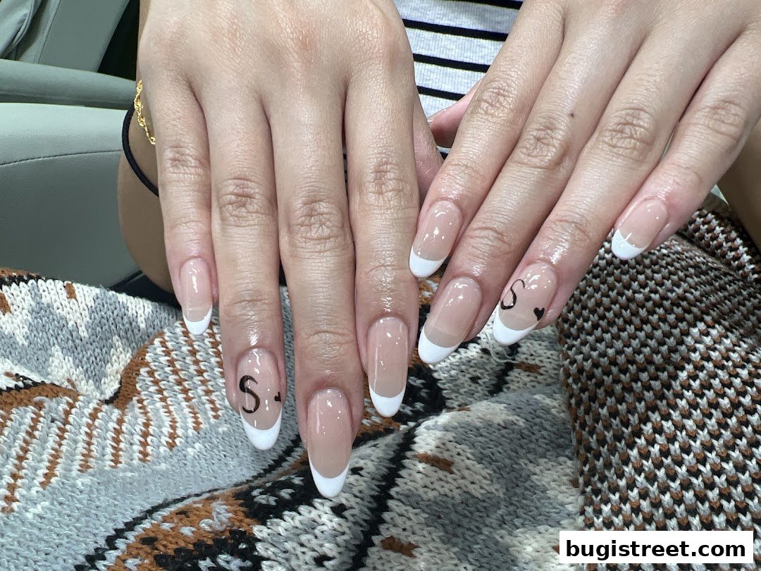 Close-up of hands with elegant French manicured nails, featuring subtle 'S' and heart designs.
