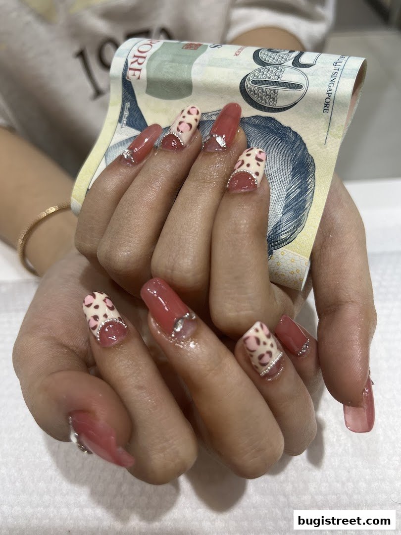 Close-up of hands with stylish pink and leopard print nails, holding a Singapore dollar bill.