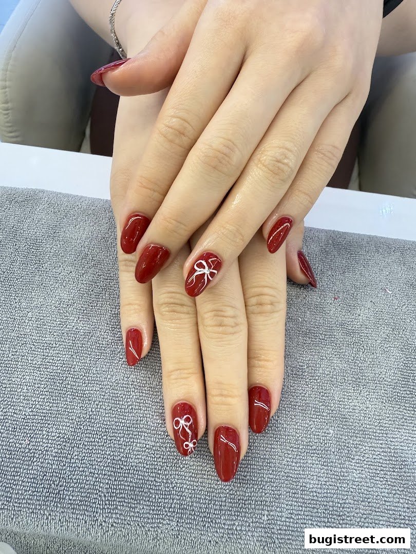 A close-up of hands with elegant red nails featuring delicate white bow designs.