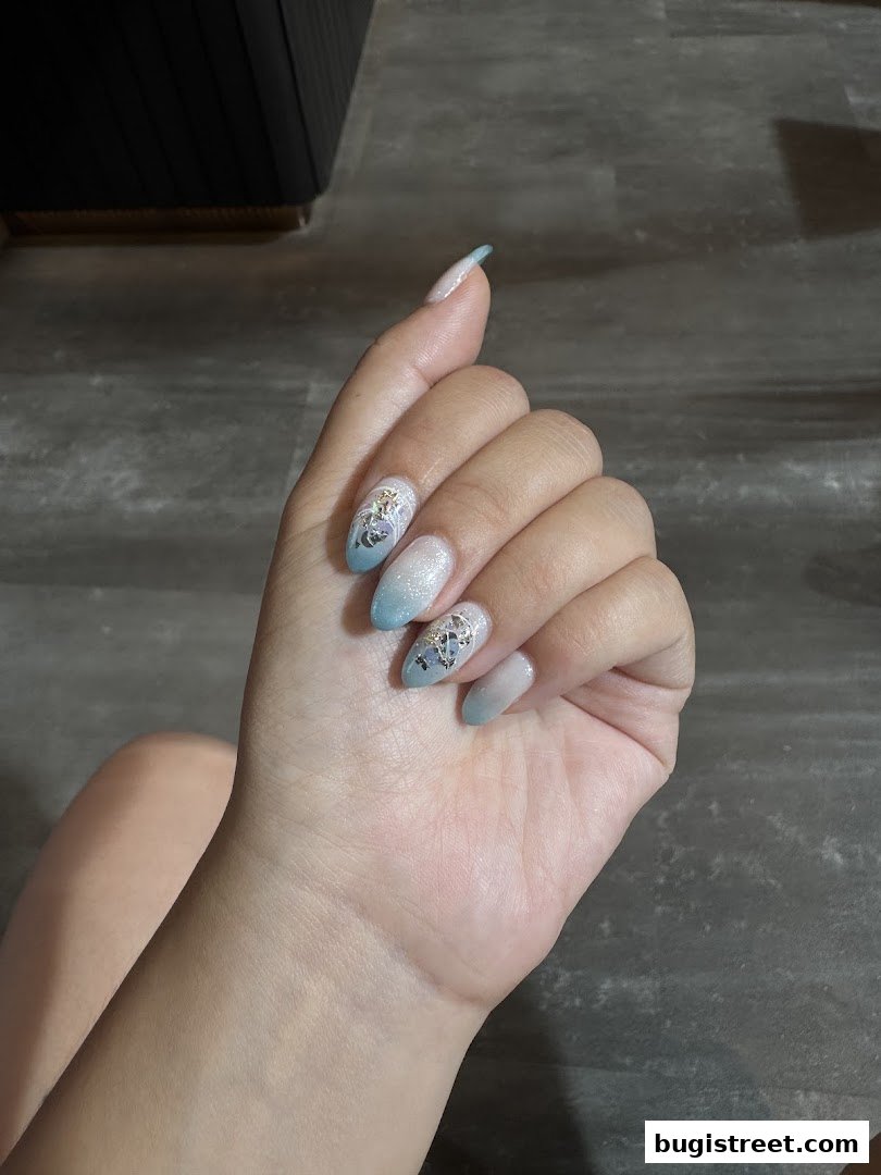 A close-up of a hand with beautifully designed nails featuring a gradient of blue and white with intricate embellishments.