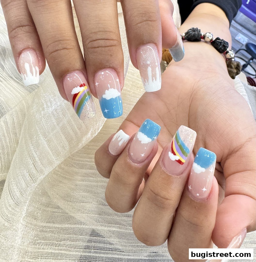 Close-up of hands with beautifully designed nails featuring rainbow and cloud motifs.